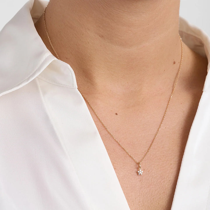 Gold necklace with small flower-shaped pendant and diamonds, front on model