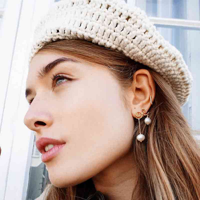 Model viser gyldne øreringe med perler, nærbillede af sideprofil, elegant stil, forside