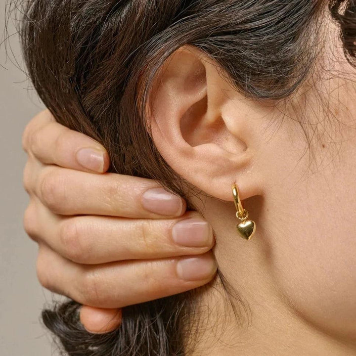 Enamel Amore Gilded Hoops shows a gold-plated heart earring in the ear of a woman. Model e376g-e376g-2