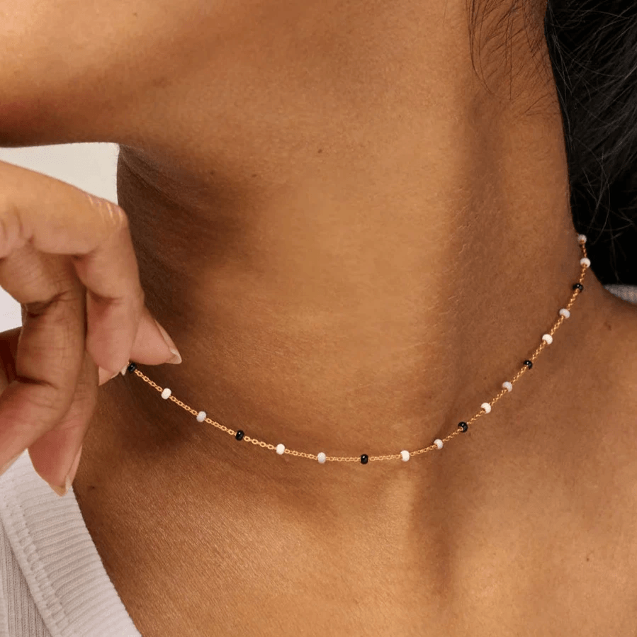 Enamel Lola Salt n Pepper Necklace is shown around the model's neck, thin chain with small white and black pearls. Model N55G-SALT PEPPER