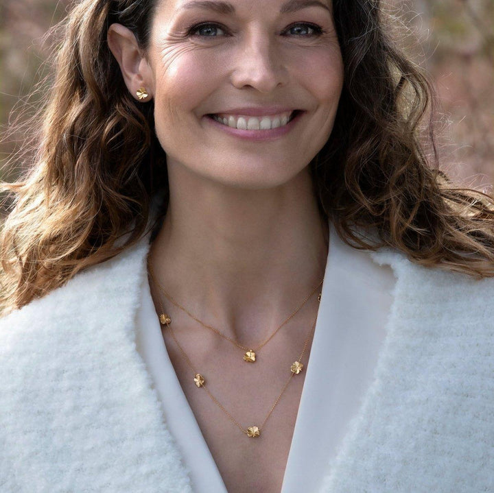Flora Danica Four-leaf clover necklace with five clovers, worn by woman, gold look outdoors. Model flc-nelo-g-2