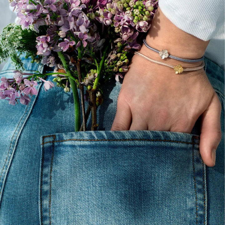 Flora Danica Firklover Silk Bracelet rose gold-plated is worn on the wrist, close to flowers and cowboy pants. Model 907-flc-silk-rose-g-001-2