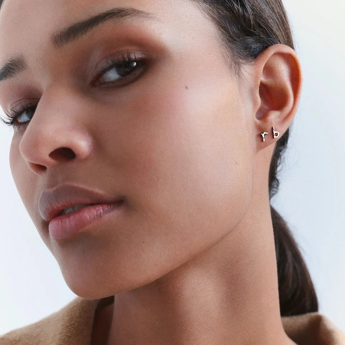 The moonstone Alphabet single letter earring A in silver is seen close to the ear of a woman. Model 101c-alphabet-001-1