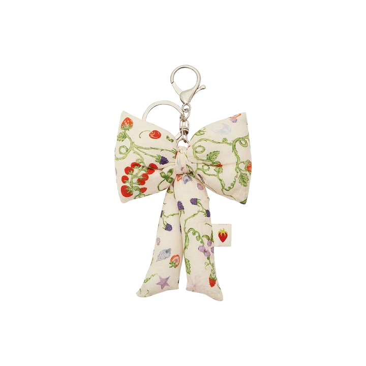 The Maanesten Fabric Bow Key Ring Garden Magic Ivory features a large floral print fabric bow and silver colored key hook. Model 4111
