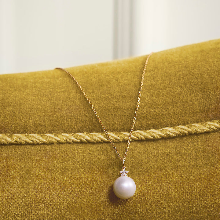 Mads Z Celeste 14kt gold pendant with cultured pearl and diamond on chain, shown on yellow velor surface. Model 1533133-2