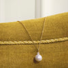 Mads Z Celeste 14kt gold pendant with cultured pearl and diamond on chain, shown on yellow velor surface. Model 1533133-2