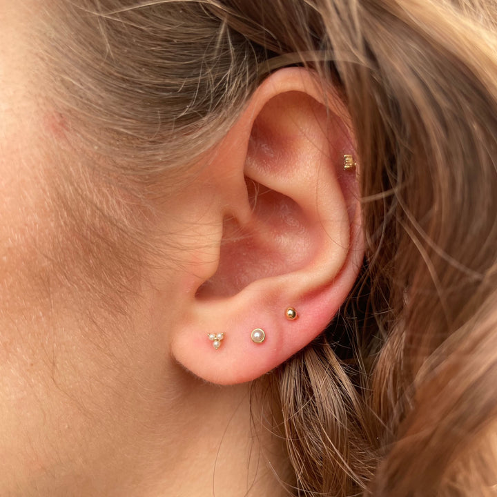 Maria Tash Pearl Trinity Stud is shown in ear, discreet gold and pearls, elegant design. Model xtrpe-yg-w3-001-2.