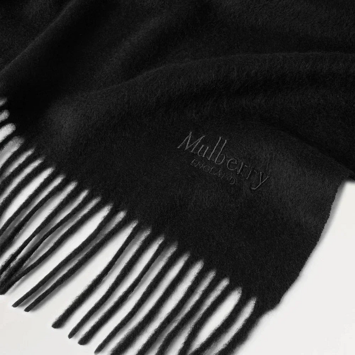Mulberry Solid Merino Whool Scarf Black shows a black merino wool scarf with fringes and discreet logo. Model vs4240947a100