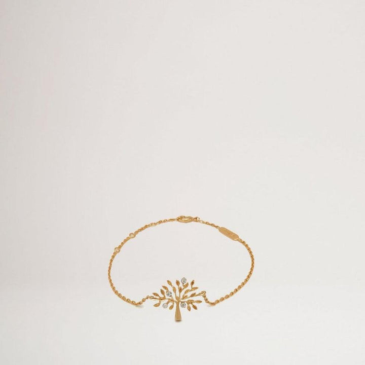 Mulberry Tree Bracelet Brass Metal shows a golden bracelet with a tree pendant in a simple, bright environment. Model QB2266000N637