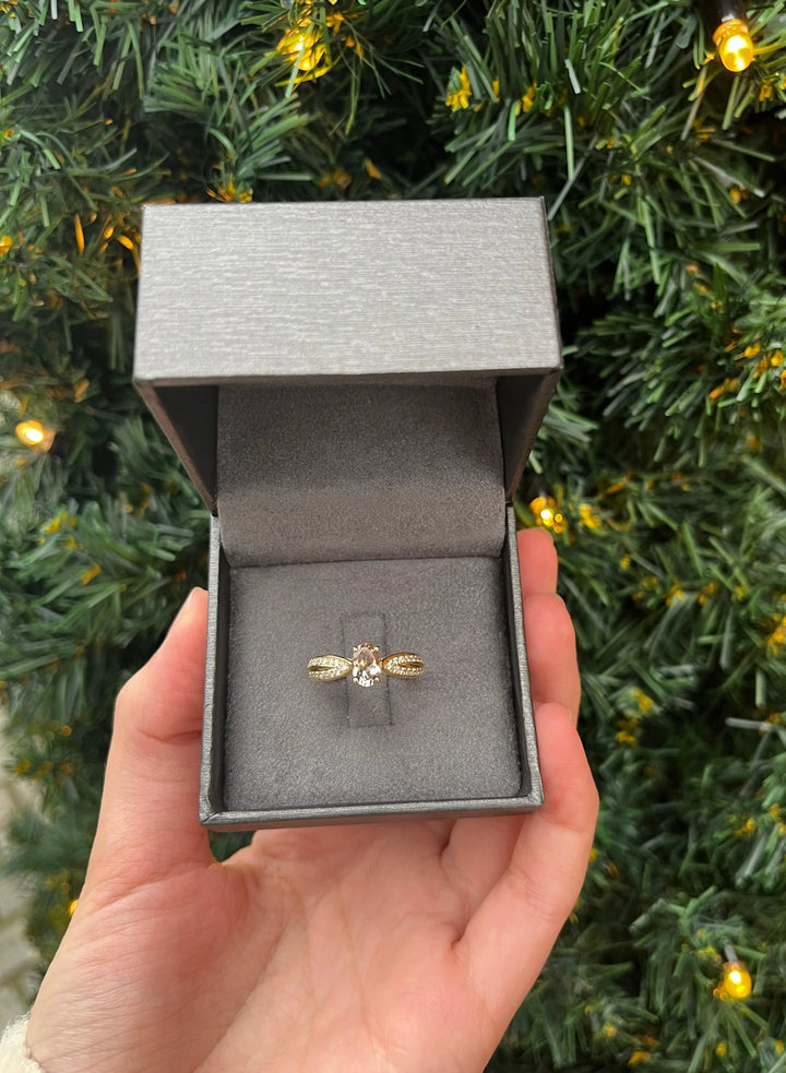 Nuran 14kt Silvia ring 0.30ct WSI presented in gray box, golden design in front of Christmas tree. Model a2455-mo-030-rg-001