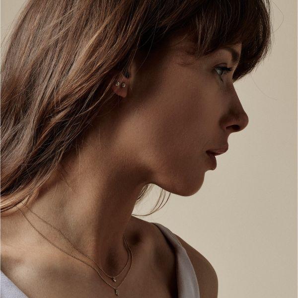 Nuran 14kt Zoe earrings appear discreetly on the ear of a woman, simple and elegant in gold. Model o2314-006rg-2.