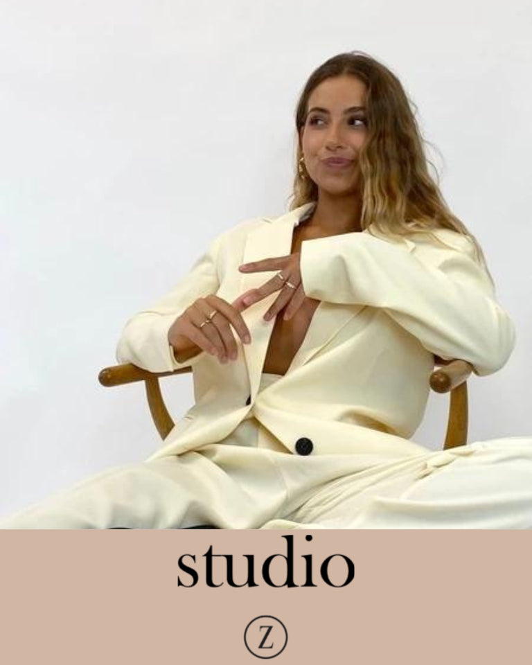 Studio Z model iført cremefarvet jakkesæt, smykker og sidder afslappet på stol, forsidefoto.