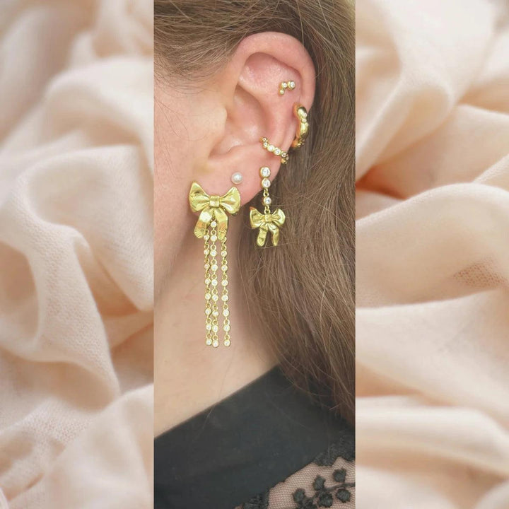 Loulou Tassel Stud shows one ear with gold colored earring in bow design with chains, detailed look. Model fw2403-2.
