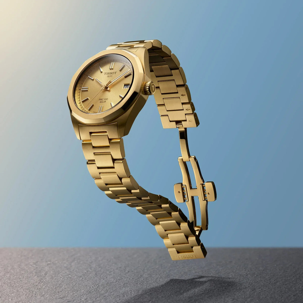 Tissot PRC 100 Solar 34mm gold PVD watch with golden dial and steel chain shown against blue background. Model T1518223302100
