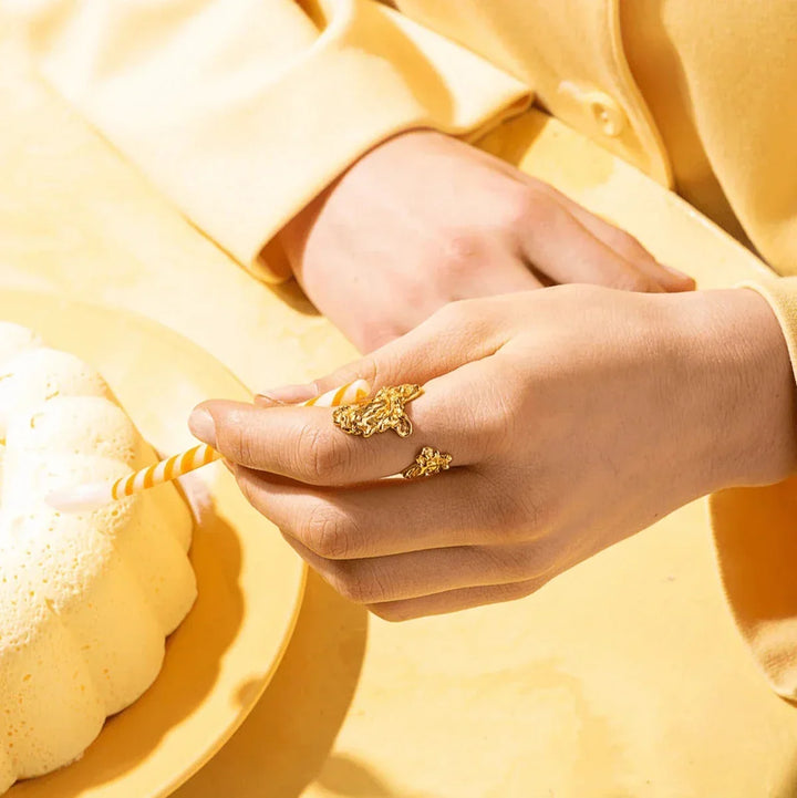 Vincent Archaic Shadow Gilded Ring appears on a hand wearing a yellow shirt, near a dessert. Model VJ105-URG-001