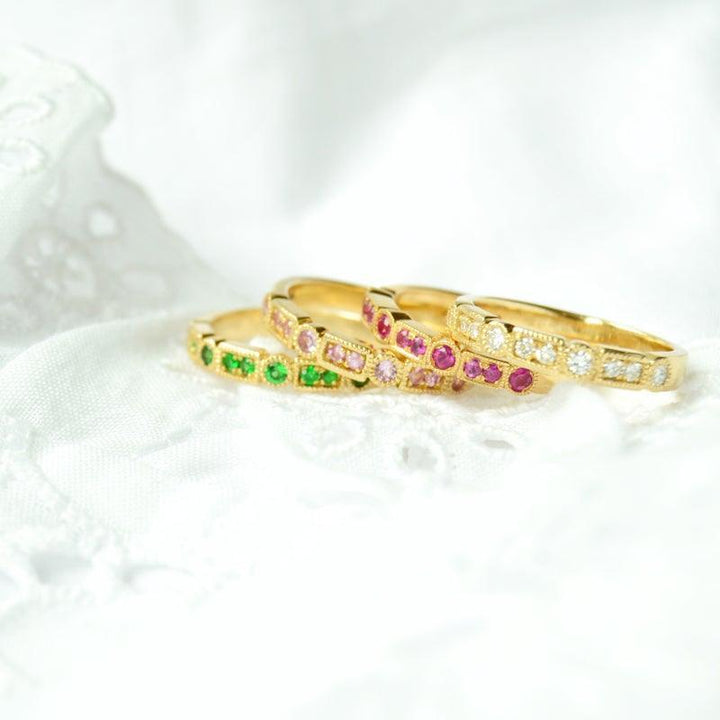 anpe-atelier-trine-ji-green-ring-14kt-gold-the ring lies at the front, elegant with green stones, in 14 kt gold on white fabric. Model 2500-001-2